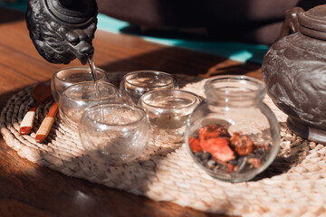 Woman pouring hot water into mugs, making tea, close-up. Tea ceremony indoors in the morning.