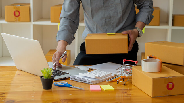 Small business owners who are just starting out, working with laptops and calculators with cardboard boxes at work, small business entrepreneurs, SME working with boxes at home, selling online, e-comm