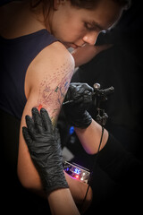 Female tattoo artist making tattoo on a men’s arm