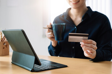 Woman's hands holding a credit card and using digital tablet for online shopping at home