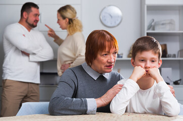 Grandma hugging upset boy during parental quarrel in home interior
