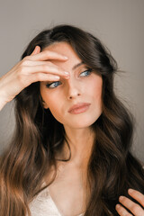 Portrait of a young brunette woman, model, looking away, picks up hair.