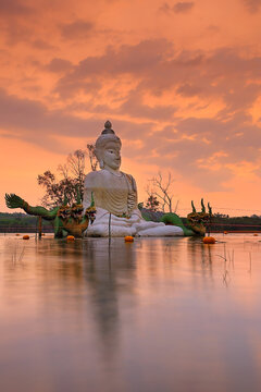 A statue of Buddha in the middle of the water at beautiful sunset at the abandoned temple at Khao Rakam Reservoir, Trat Province