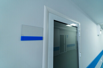 White nameplate near the door. Emergency door in white corridor of hospital.