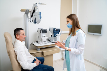 Fototapeta premium Young professional doctor in medical uniform talking with patient. Beautiful nurse in medical mask treating about patient health.