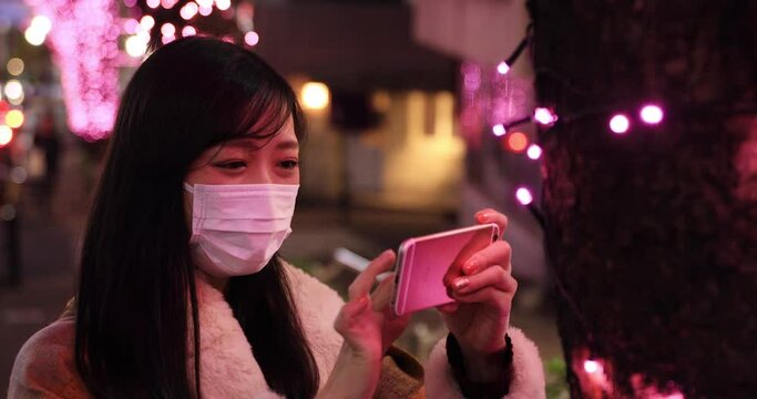 A Japanese mask woman shooting by smartphone at illuminated street close shot