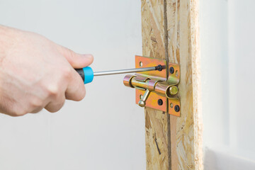 Young adult man hand using manual screwdriver and screwing new slide lock of greenhouse door....