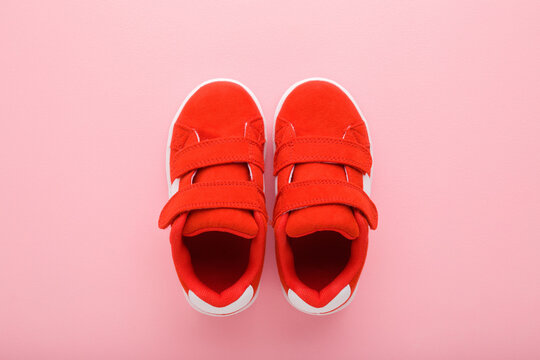 New Red Sport Shoes For Little Kid On Light Pink Table Background. Pastel Color. Baby Footwear. Closeup. Top Down View.