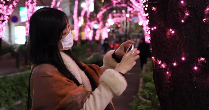 A Japanese mask woman shooting by smartphone at illuminated street close shot