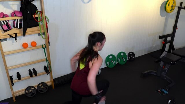 Young athletic woman performing lunges alone in home-gym to stay fit during quarantine - Crane shot low to high