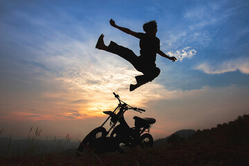 Fototapeta na wymiar Beautiful landscape shadows of an old motorbike on the top of the mountain with Young man jumping kung fu pose, the beautiful sky