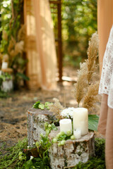 White paraffin candles on wood stumps near wedding altar.