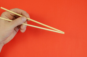 A man's hand holds wooden chopsticks against a red background.