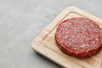 Raw beef burger patty on wooden board