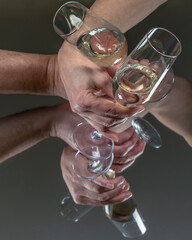 A male and female hand cross each other holding a glass of sparkling wine on a reflecting mirror surface