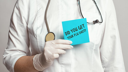 Cropped view of doctor in a white coat and sterile gloves holding a note with words - Did you get your flu shot