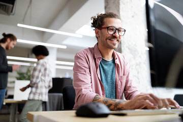 Young hipster man smiling while working on computer desk in office