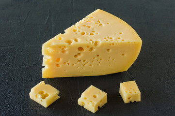 Radamer cheese on a black concrete background. triangular piece of yellow cow's milk swiss cheese with holes