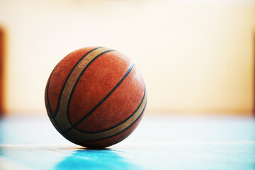 A human foot rest on the basketball on the concrete floor. Photo of one basket ball and sneakers in a wooden floor.