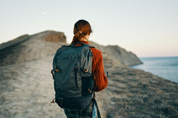 beautiful woman traveling in the mountains with a backpack on her shoulders near the sea