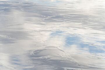 Part of a shiny, frozen lake, with reflection of the blue cloudy sky. Background, backdrop