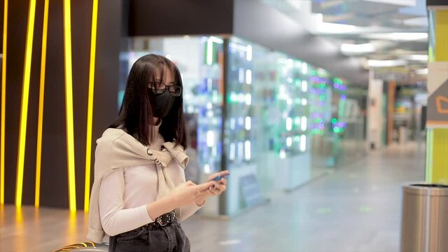 Girl in a shopping mall communicating in a smartphone with a face mask. Modern communication, entertainment, shopping. Woman modern, the concept of being in public places of public use.