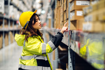 Portrait of smiling asian engineer in helmet woman order details and checking goods and supplies on shelves with goods background in warehouse.logistic and business export