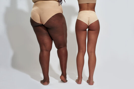 Back view of legs of two women in beige underwear with different body shape standing isolated over gray background