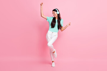Full size photo of young happy positive excited girl listen music in headphones dancing isolated on pink color background