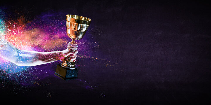 Hand holding up a gold trophy cup against dark background