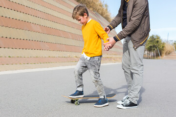 Father is teaching his son to ride a skateboard, outdoors