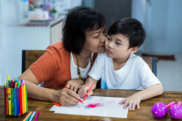 Grandmother with grandson drawing together at home. Grandmother helping little grandchild doing homework.