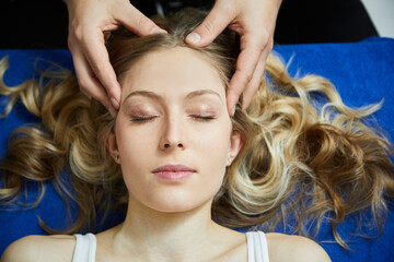 Blonde young pretty woman gets a facial massage. Her eyes are closed and shine at the viewer. Her curly hair rests on a blue yoga mat. Turn off and unwind. Top shot. Day.