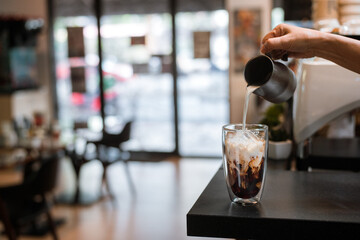 Barista pouring milk into a glass of iced coffee