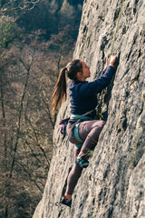 Woman climbs with steady focus on the grips on the wall.