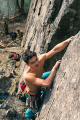 Young shirtless male climber starts climbing on limestone cliff.