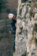 Man climbs vertical wall with helmet with blurred rock in the foreground.