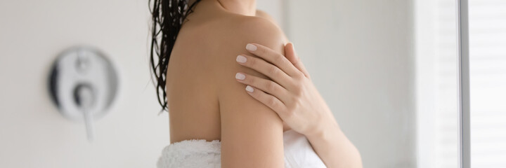 Young woman wrapped in bath towel touching shoulder soft skin, enjoying cosmetic effect of...