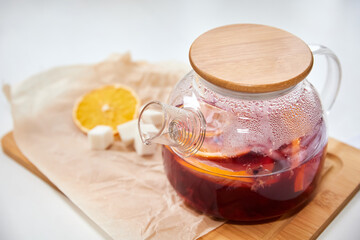 Berry tea with orange in a transparent teapot on light background. Close-up, selective focus