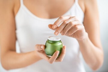 Woman applying moisturizer from jar