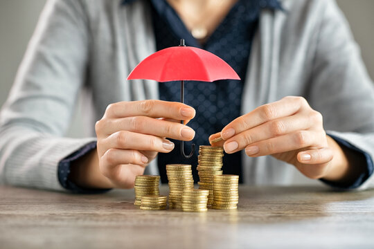 Hands protecting pile of coins with umbrella