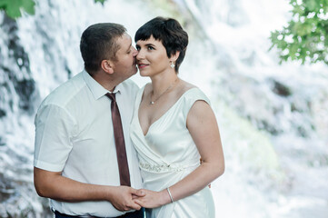 Naklejka premium The bride and groom stand against the background of a waterfall. Newlyweds on the background of a waterfall