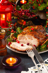 Roast pork neck in Christmas style. Dark navy blue background. Christmas accessories. Candles and lanterns in the background.