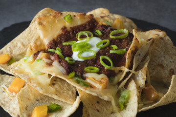 Close up of a plate of nachos with vegetables, cheese and beans