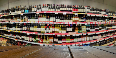Blurred image of a liquor store with drinks. Wine bottles on the shelves. In the foreground is a table or counter.