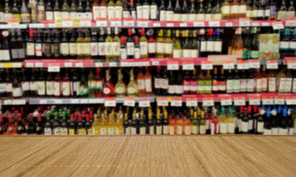 Blurred image of a liquor store with drinks. Wine bottles on the shelves. In the foreground is a table or counter.