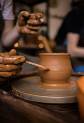 close-up of a man's hands in clay making a pattern on a clay bowl in a room