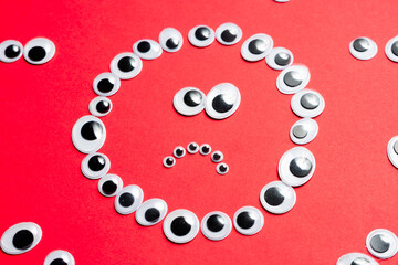 Sad smiley face from toy eyes in the surroundings of other eyes on an red background