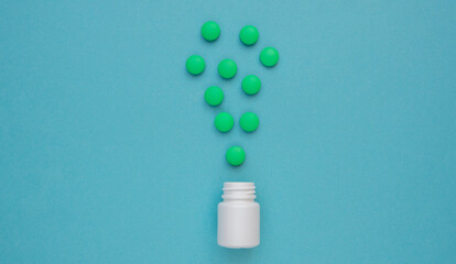 Many pills and many multicolored green pills are poured out of the pill jar on a blue background. Medicine and health concept. Vitamins, antibiotics. view from above. Flat lay