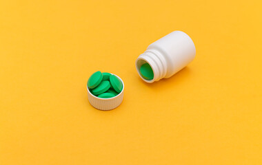 White pill jar and green pills on a yellow background. Medicine and health concept, taking metered pills. Vitamin complex vitamins for health, beauty and youth. Antibiotic treatment. copy space. 